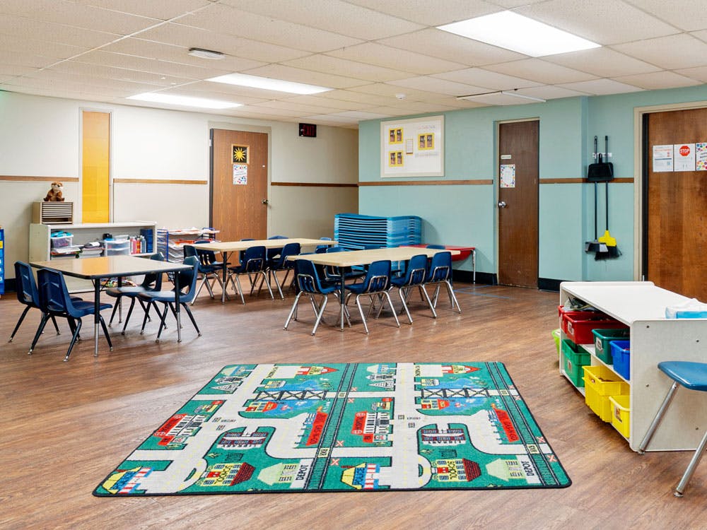 Empty classroom with small tables and chairs and a play rug