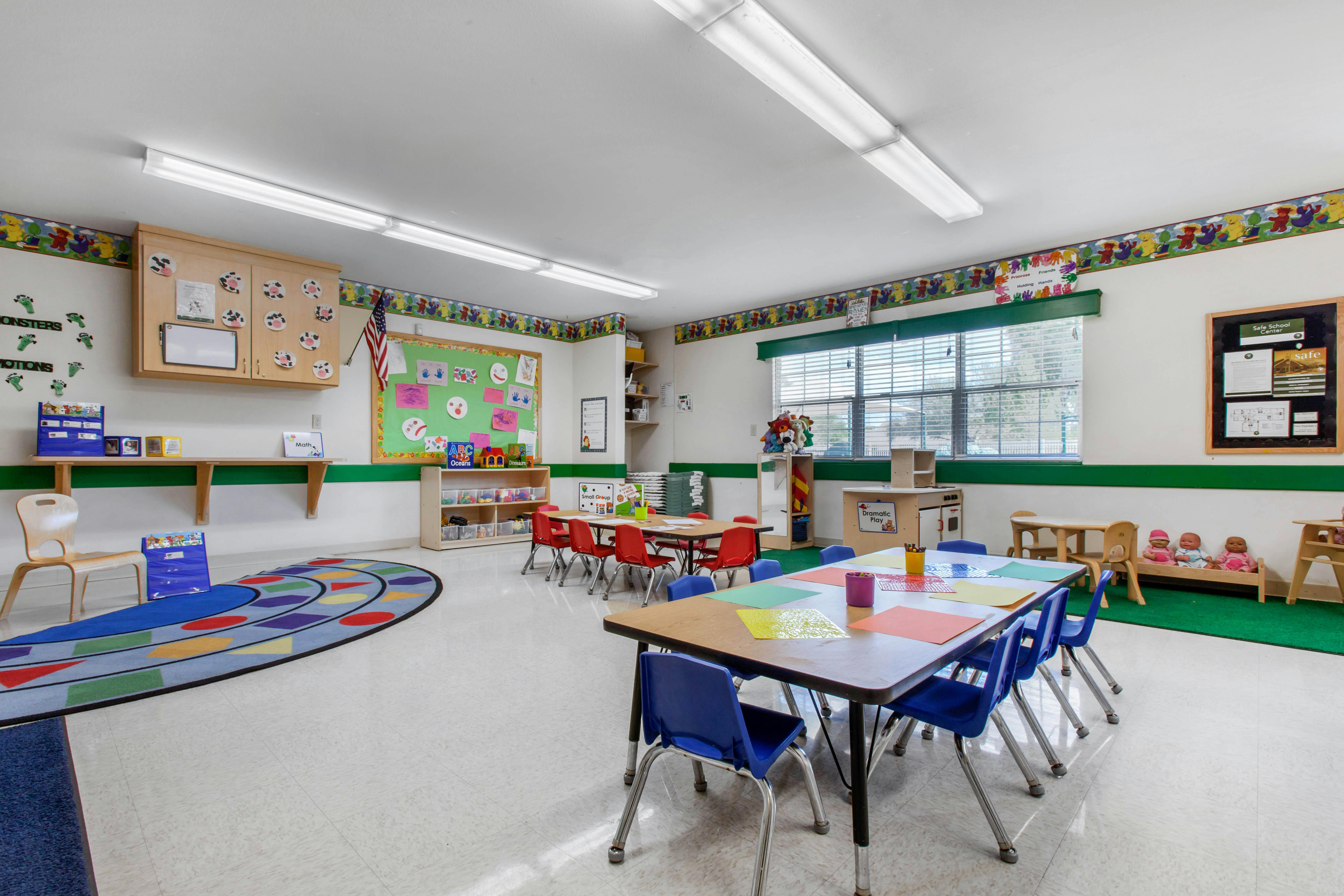 Classroom with small tables and chairs, toys, and a colorful rug