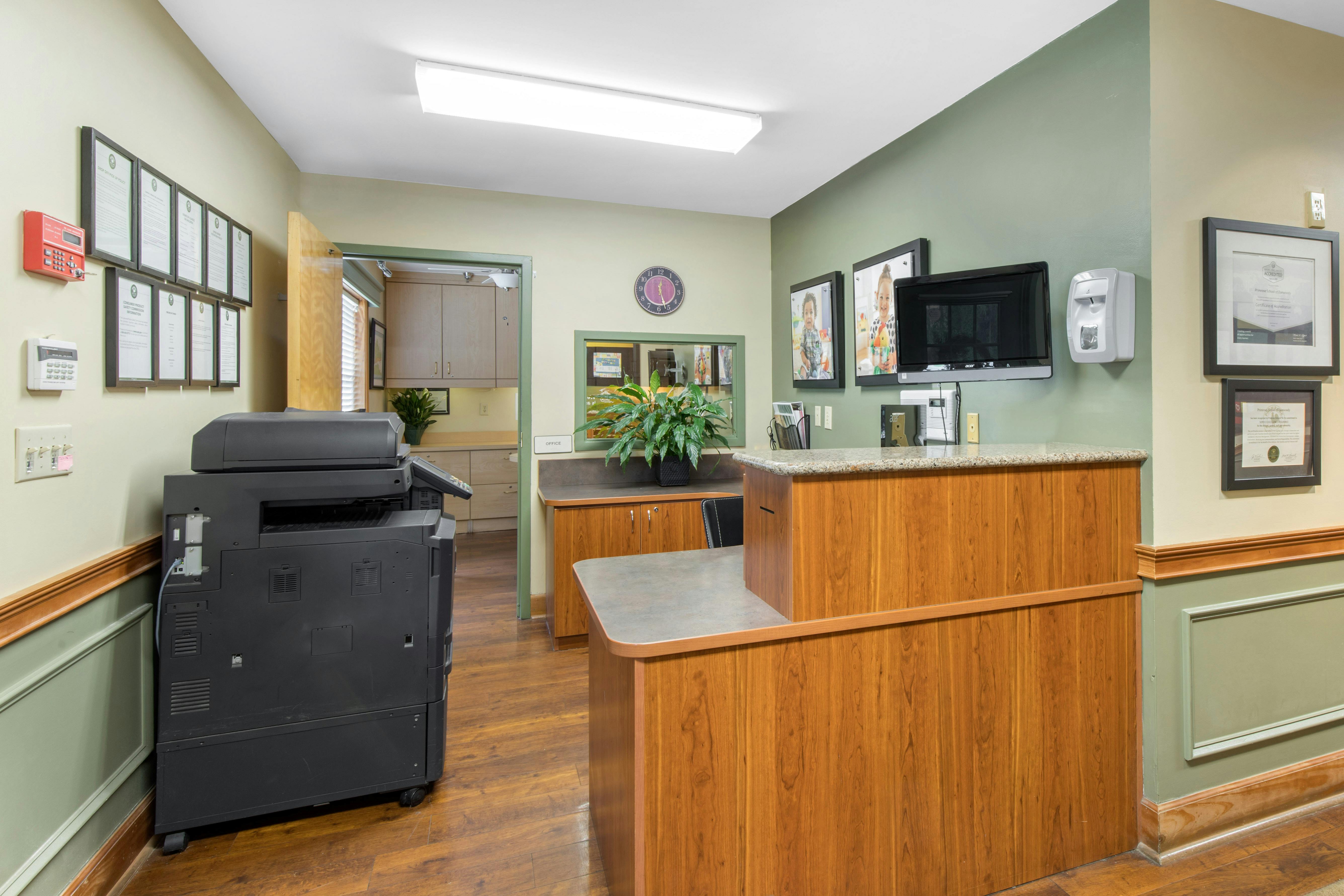 Reception area with a large printer, a wooden counter, and framed certifications