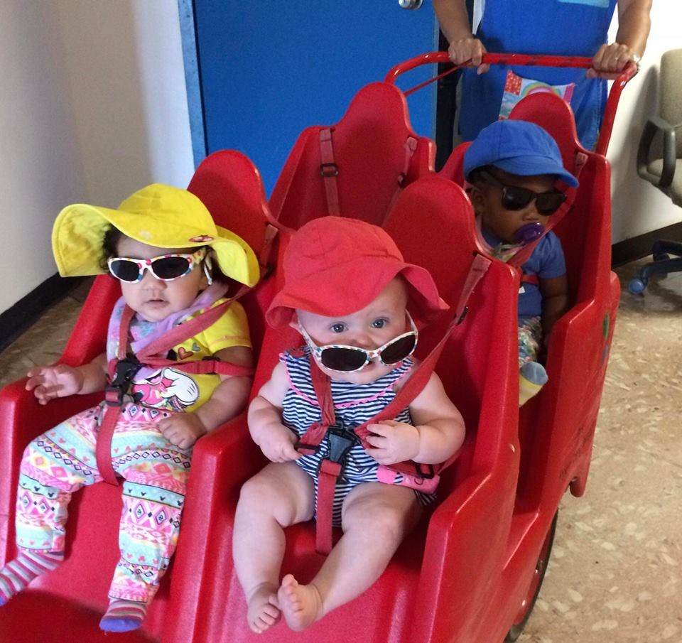 Three children in hats and sunglasses sitting in a red multi-seat stroller