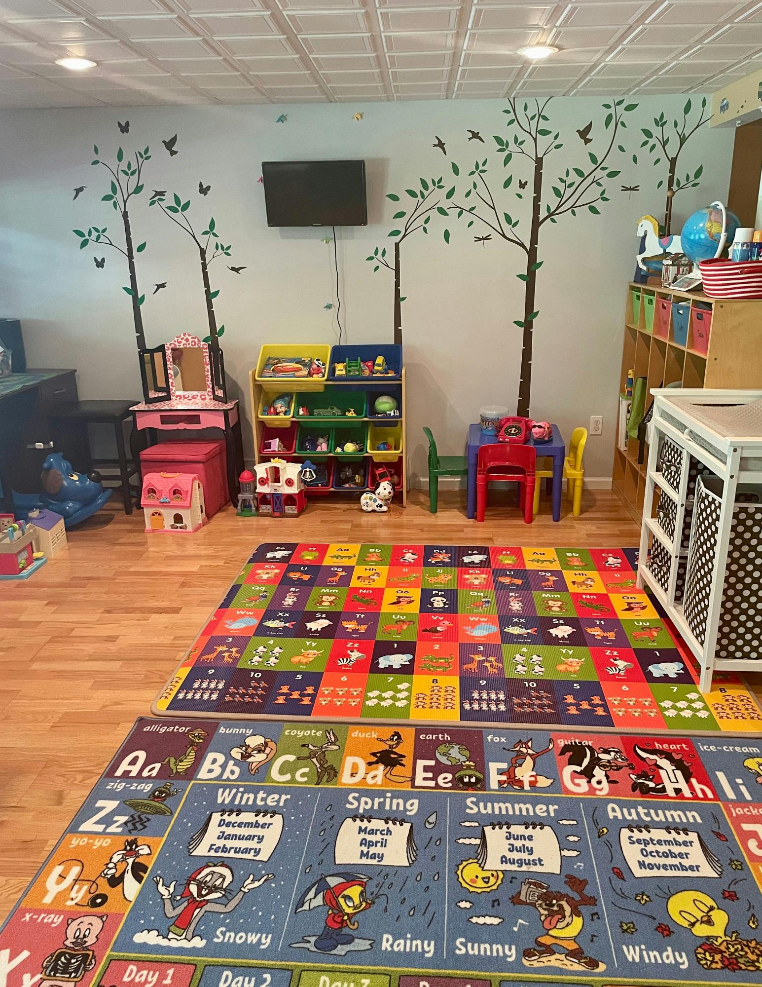 Playroom with colorful rugs, toys, and tree decals on the wall