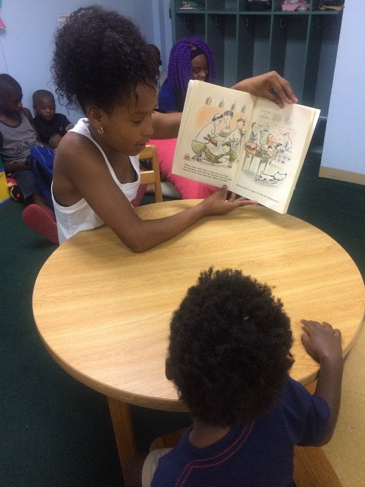 Person reading a book to a child at a table