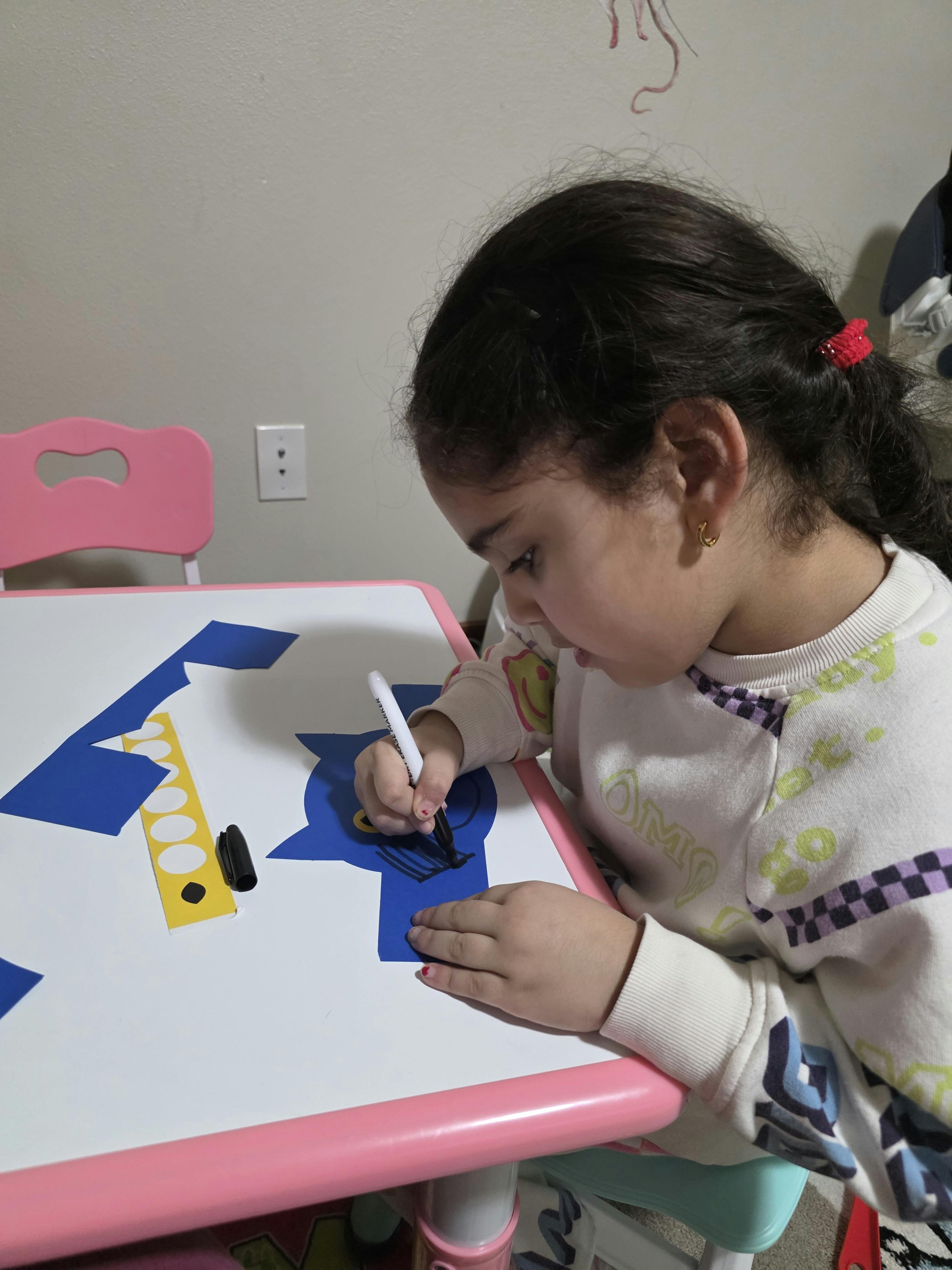 Child drawing on blue paper cutouts at a table