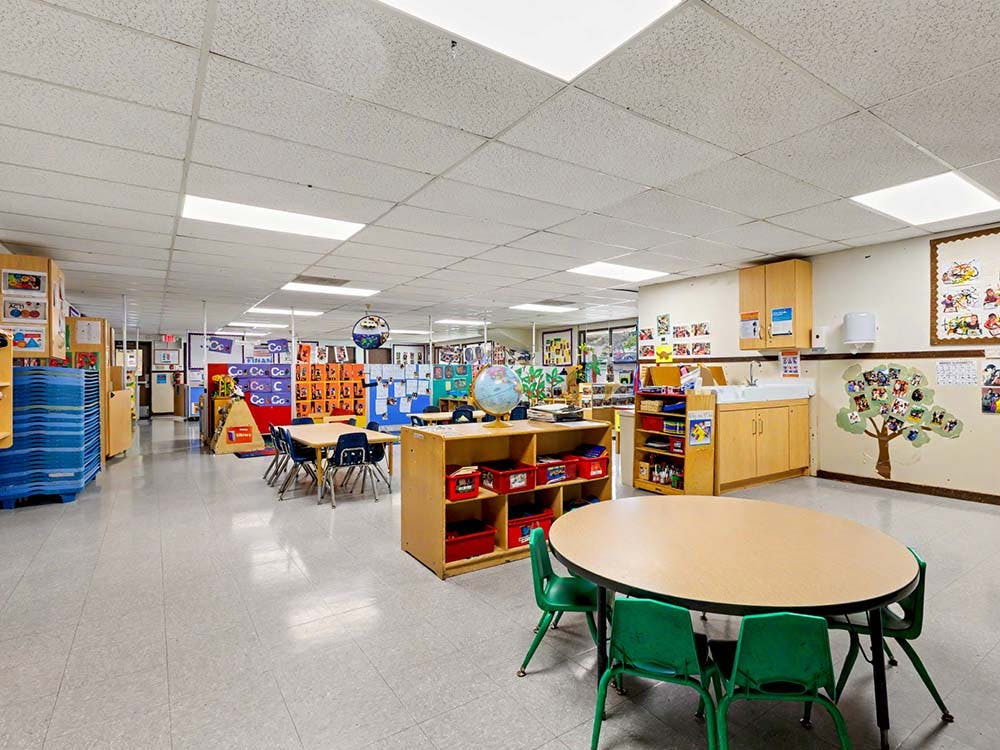 Empty classroom with small tables and chairs, storage units, and a sink