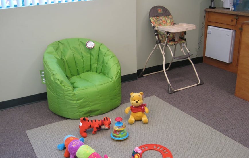 Green bean bag chair, high chair, and toys on a rug