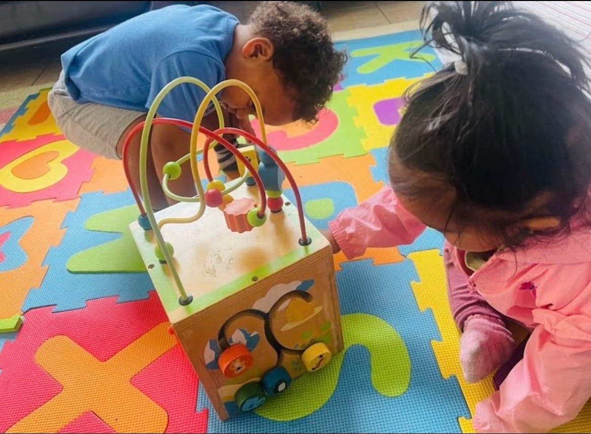Two children playing with a wooden activity cube on a foam mat