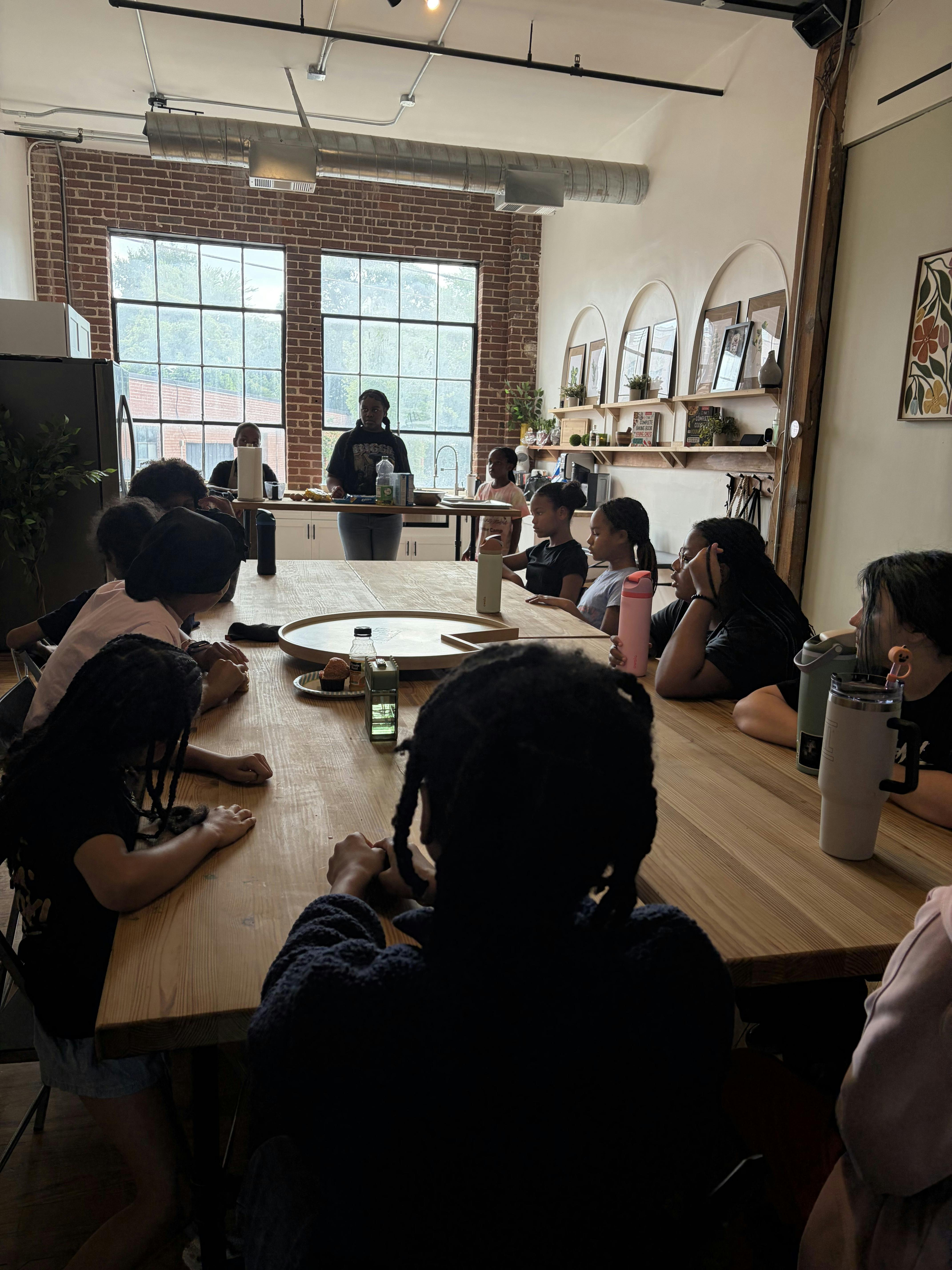 Group of children and a person listening at a large wooden table