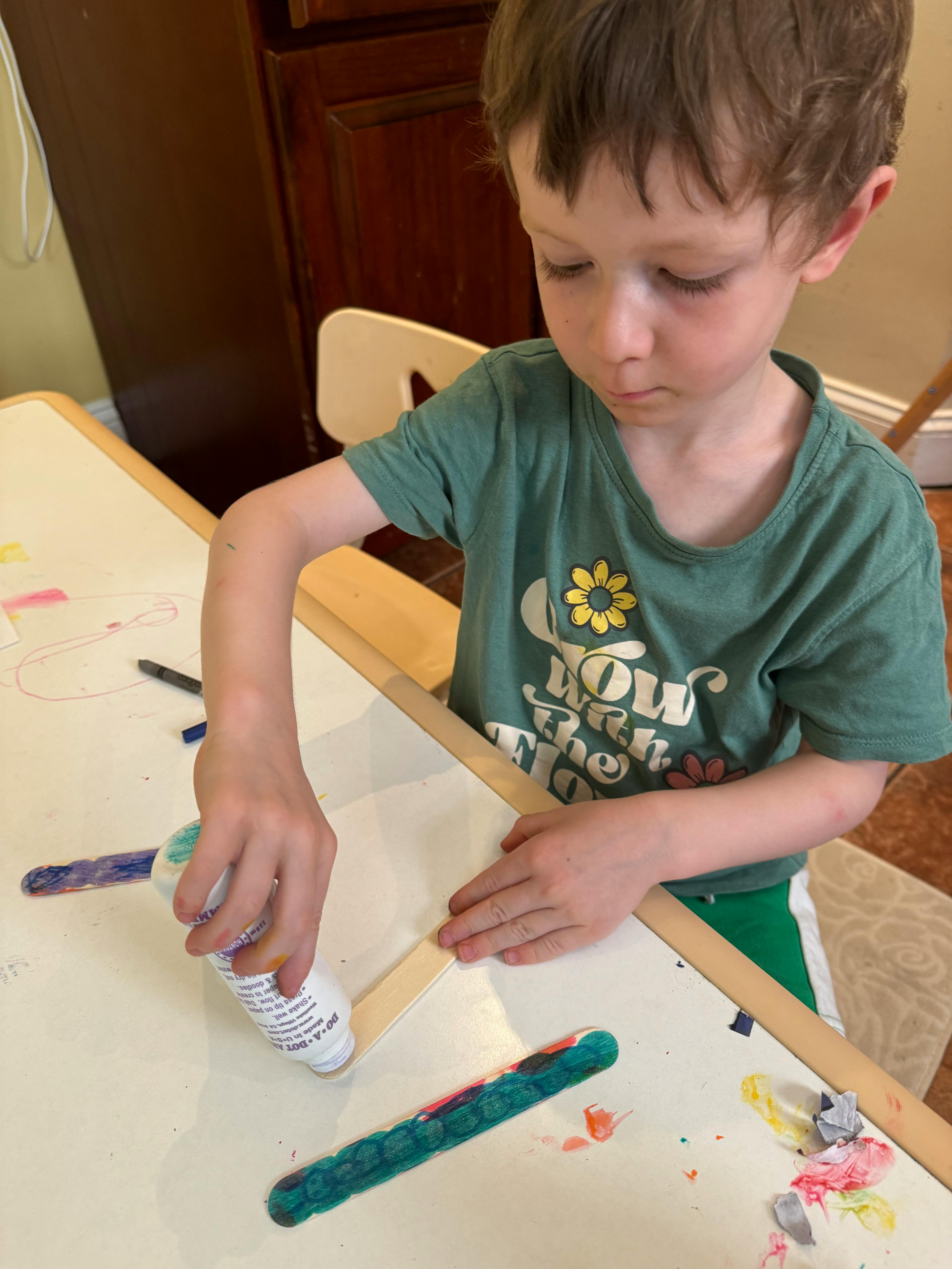 Child applying glue to a craft stick at a table