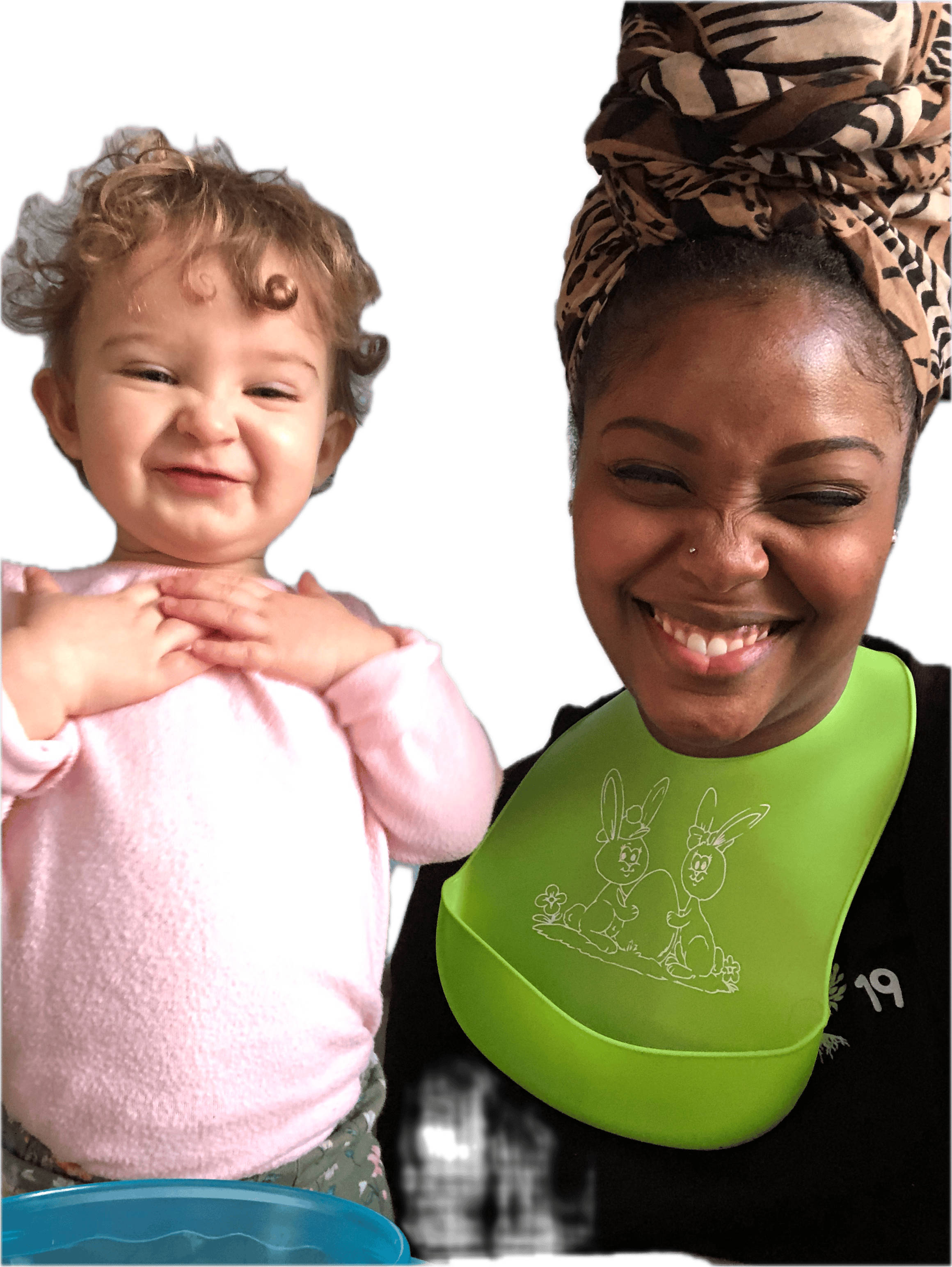 A person wearing a patterned headwrap and a green bib next to a curly-haired child