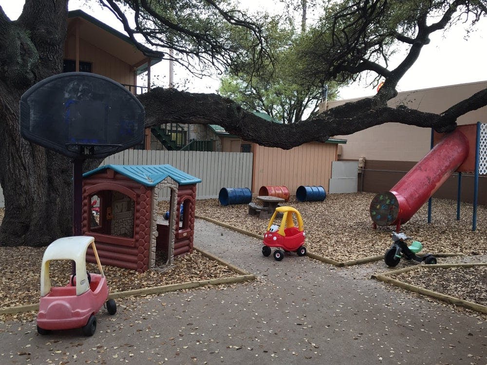 Playground with playhouse, slide, and toy cars under a large tree