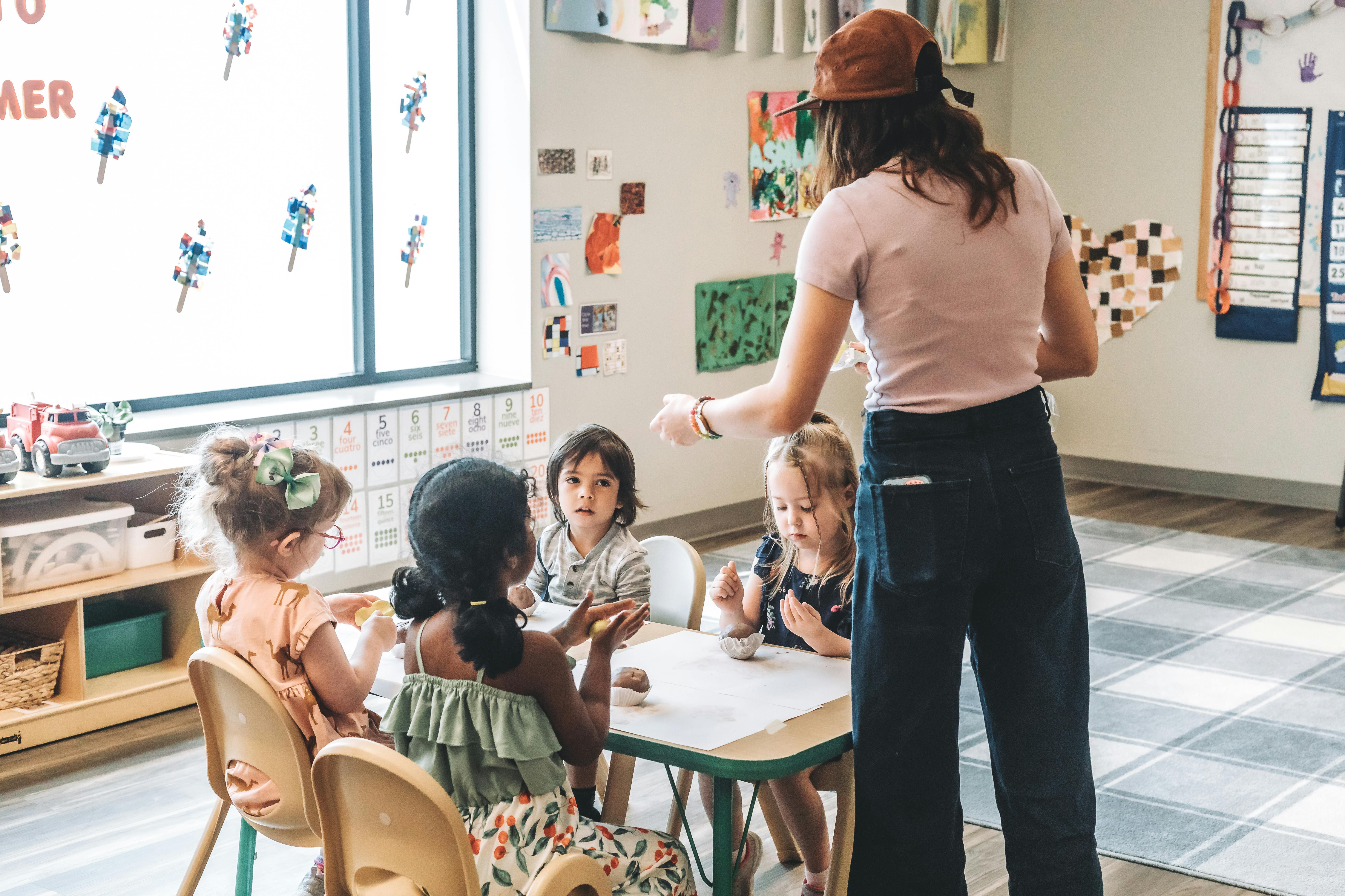 Adult person standing with four children seated at a table in a classroom
