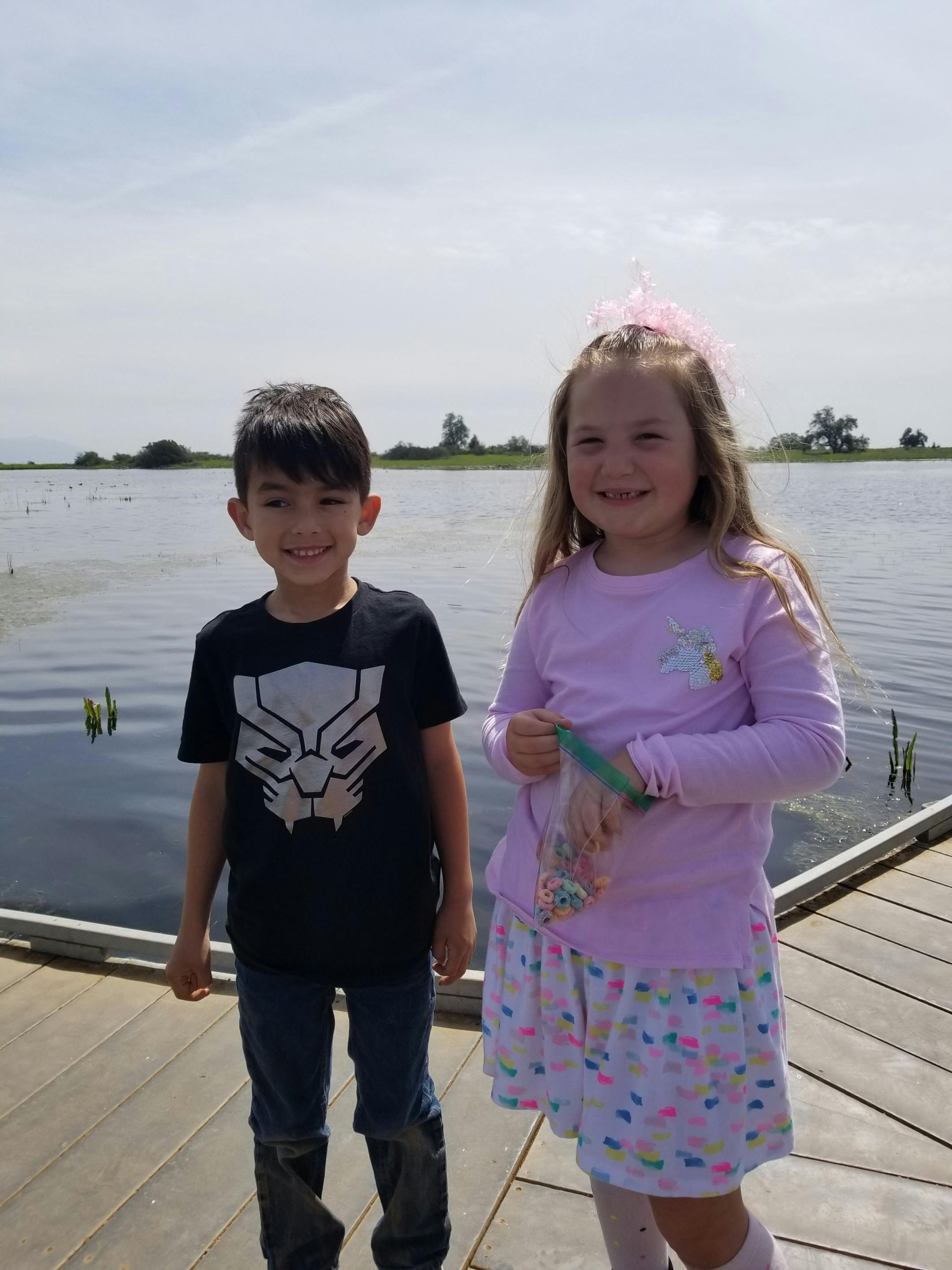 Two children standing on a dock by water