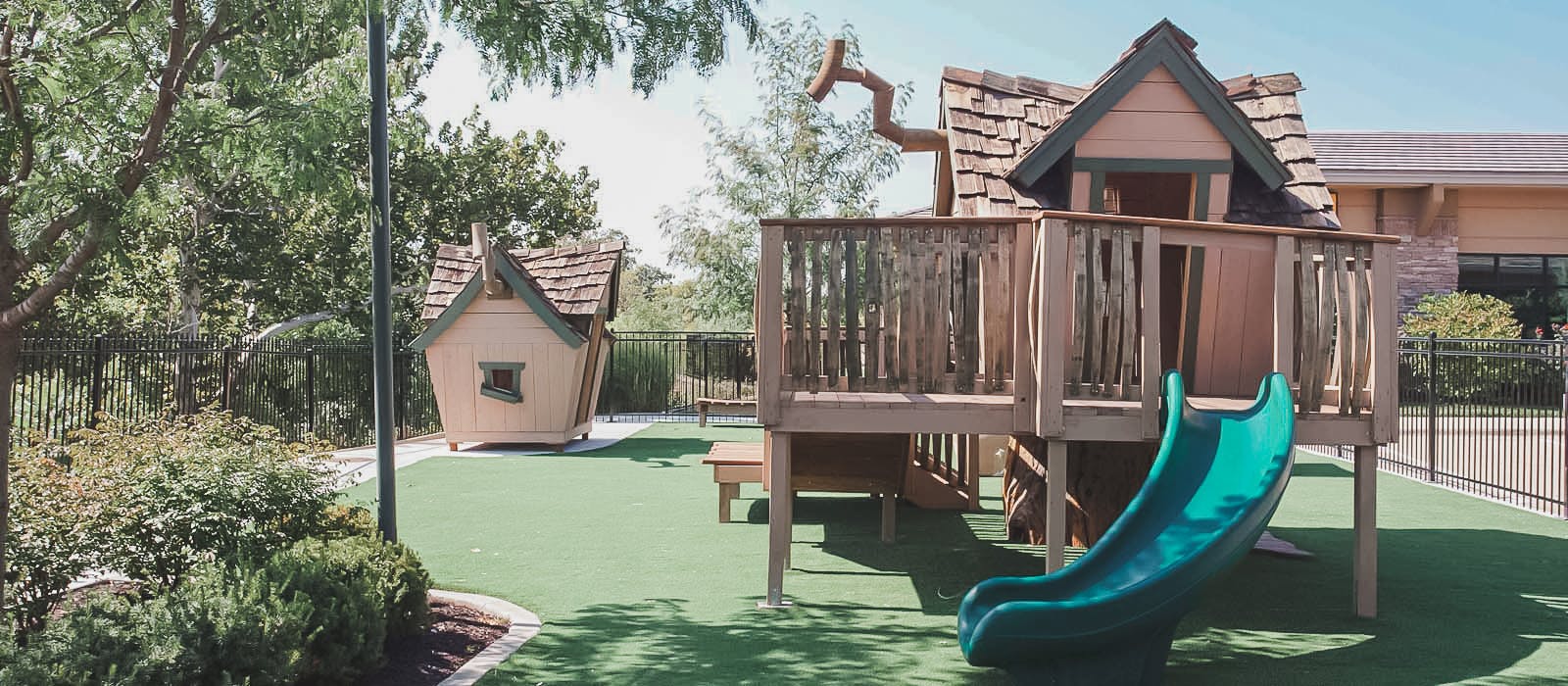 Playground with a wooden playhouse and slide on artificial turf