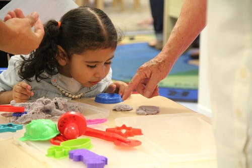 Child playing with kinetic sand and molds, person pointing at the sand
