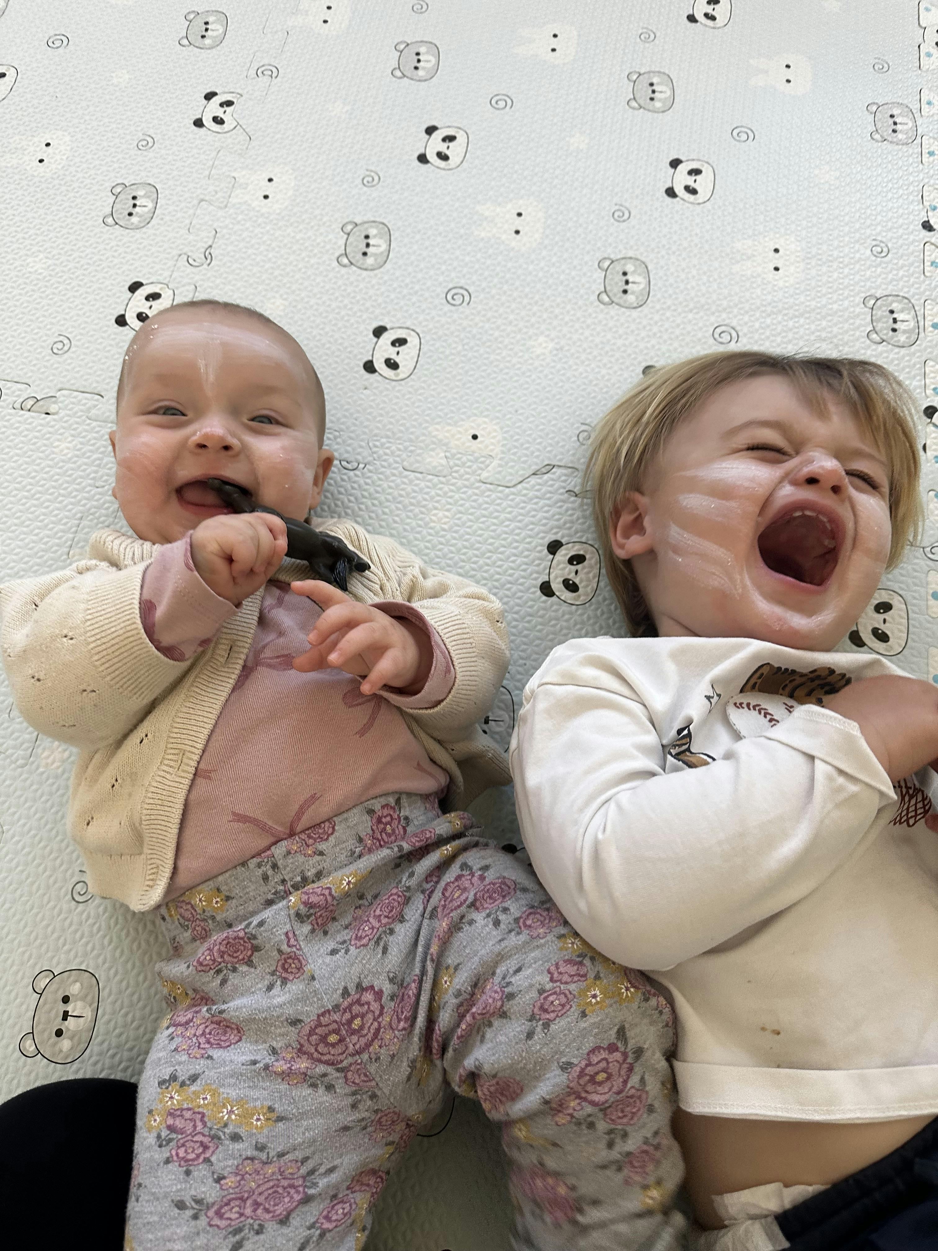 A child and a baby with white cream on their faces on a panda mat