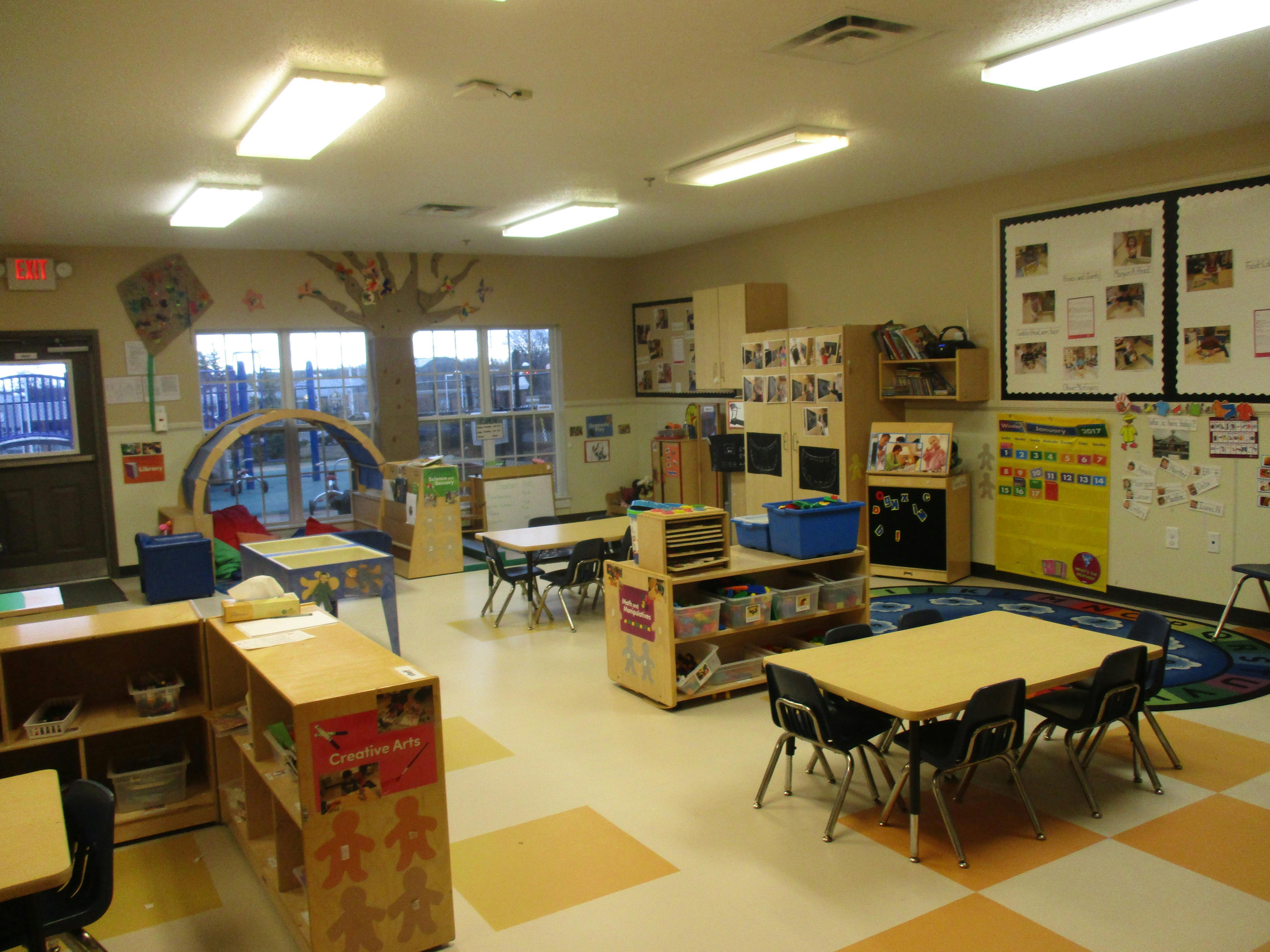 Classroom with tables, chairs, shelving units, and a calendar on the wall