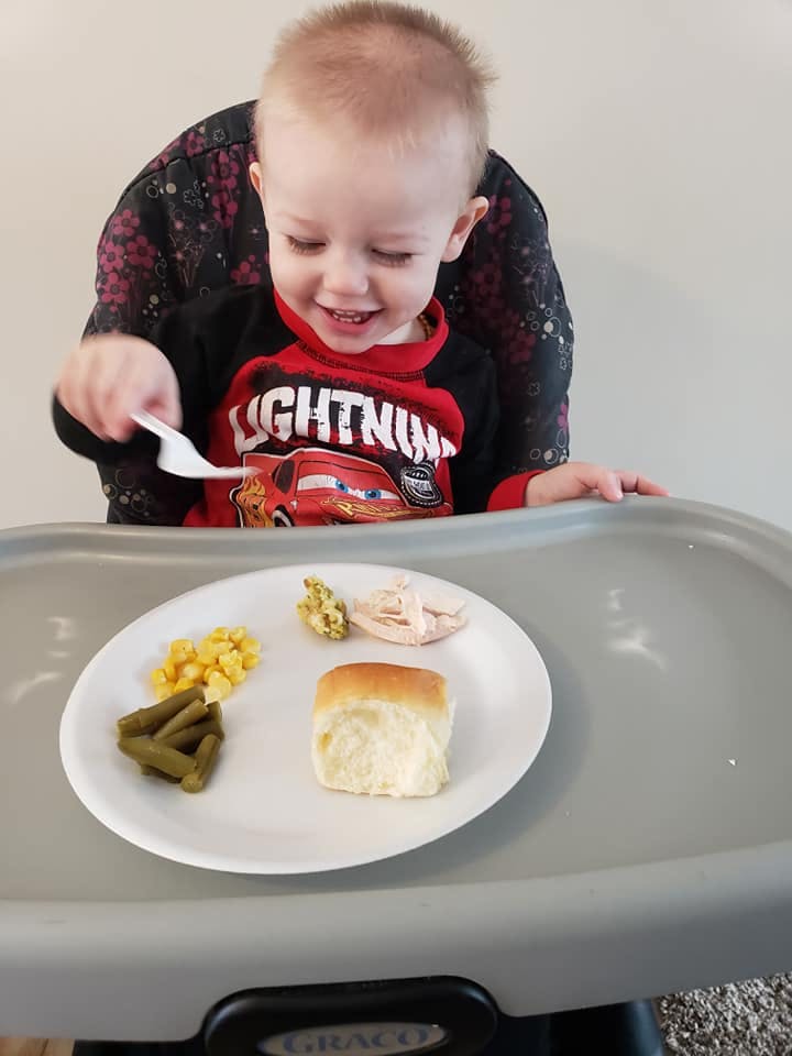 Child in a high chair holding a fork over a plate of food