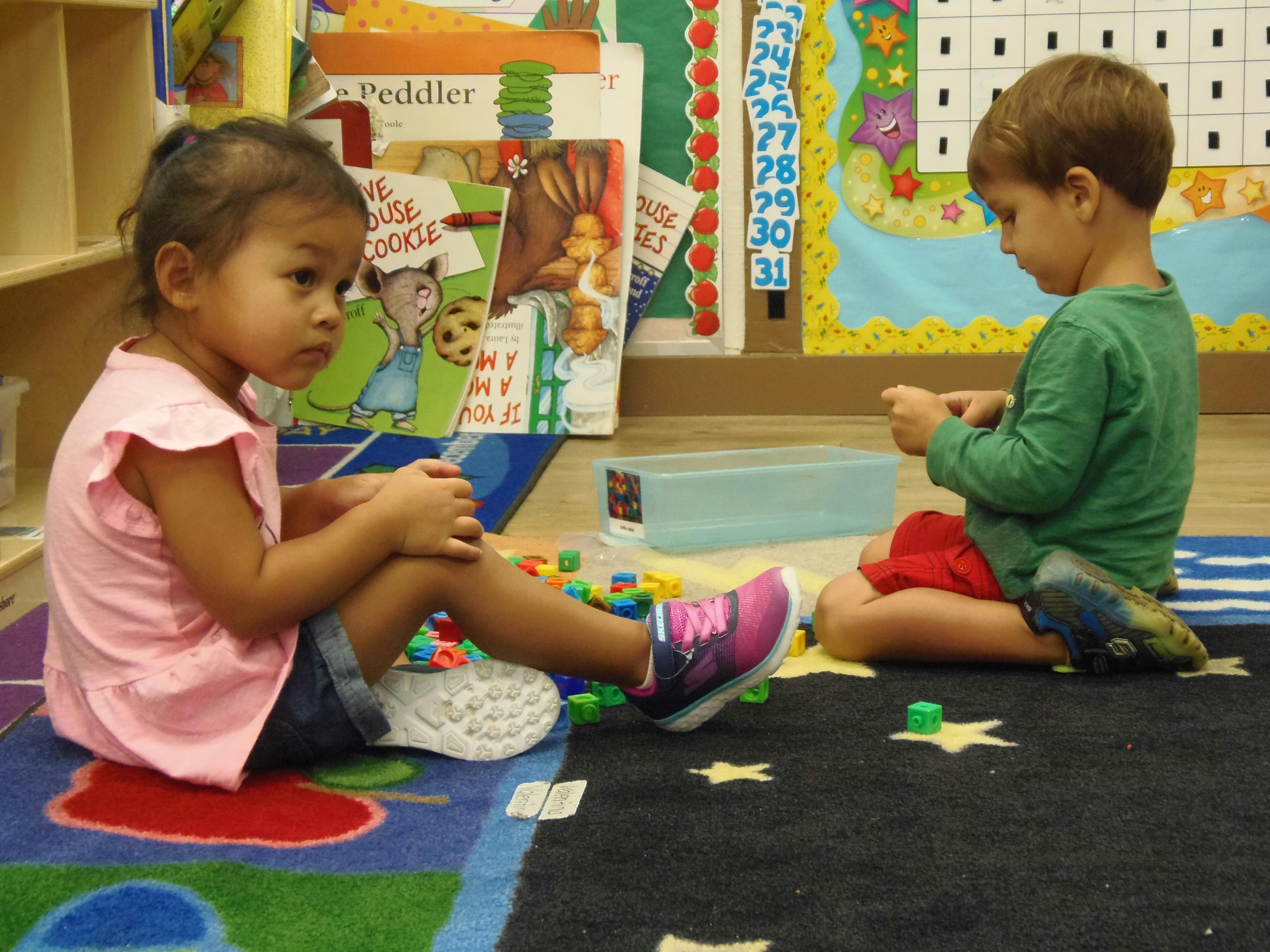 Two children sitting on a rug playing with small blocks