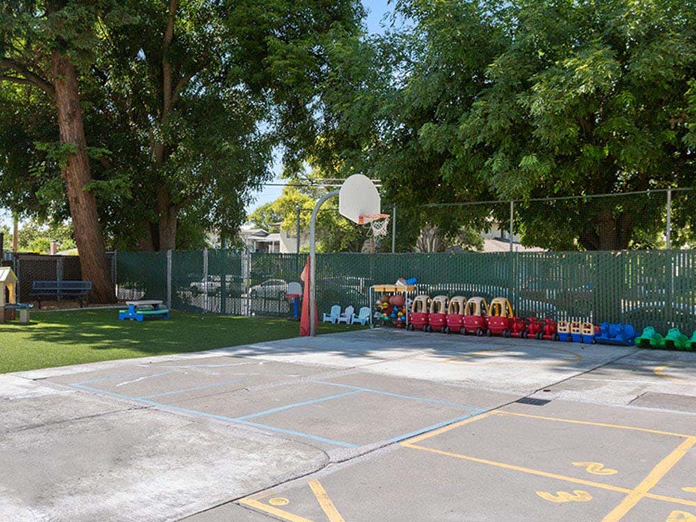 Outdoor play area with a basketball hoop, small ride-on toys, and artificial grass