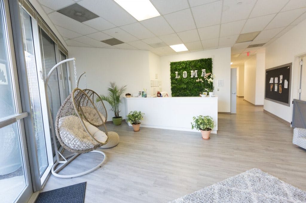 Lobby with a white reception desk and a green wall with "LOMA" text