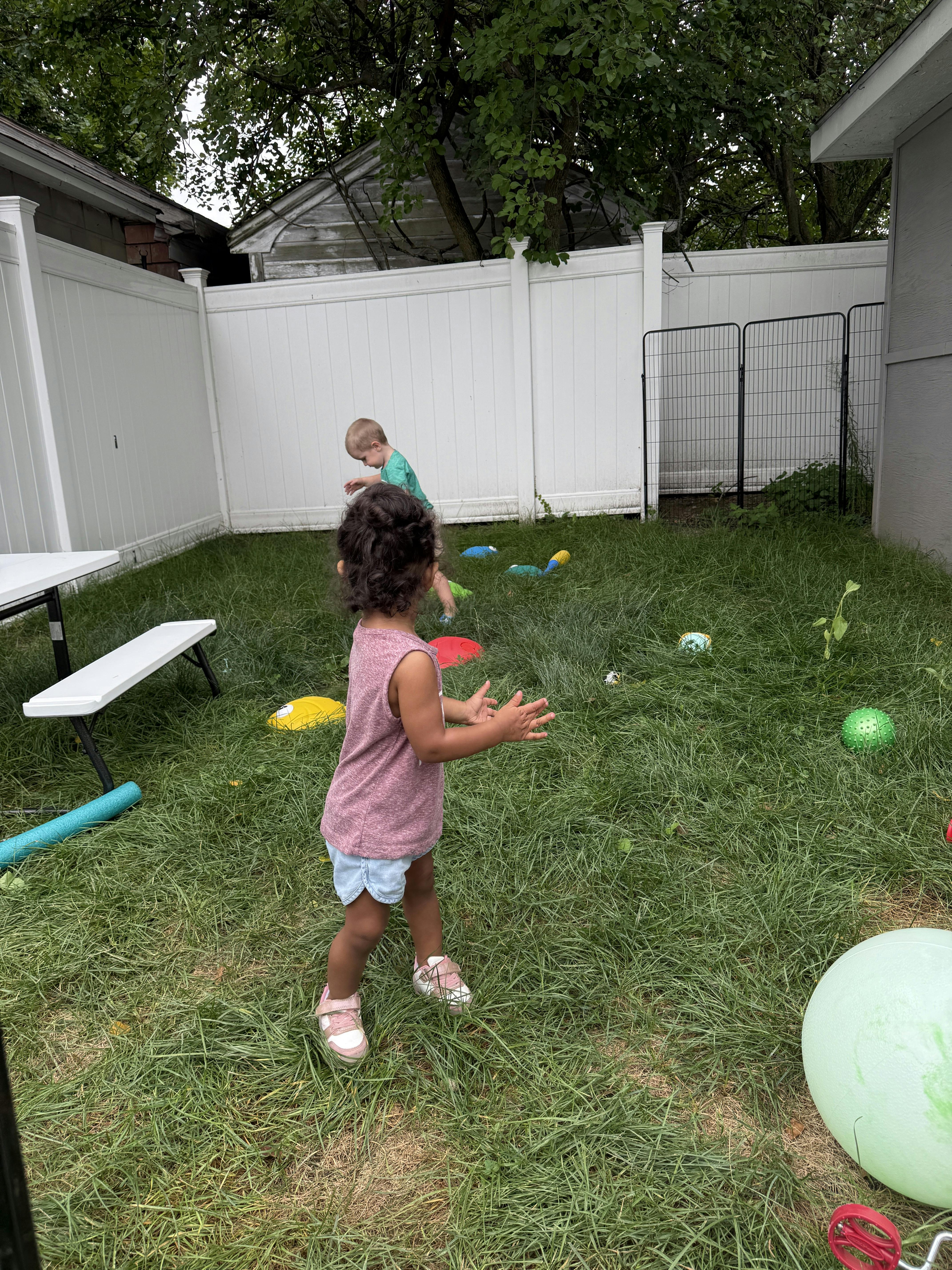 Two children playing with balls in a grassy backyard