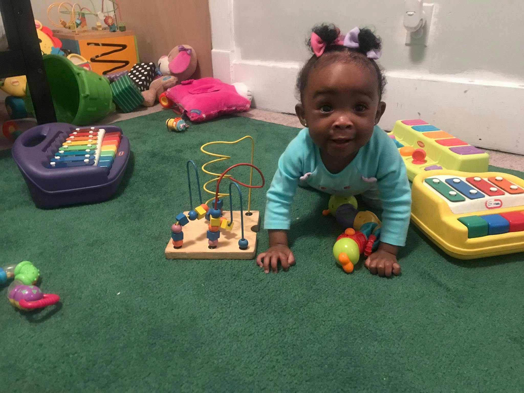 Child crawling on a green carpet surrounded by toys