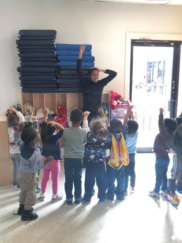 Adult leading a group of children in an activity with arms raised