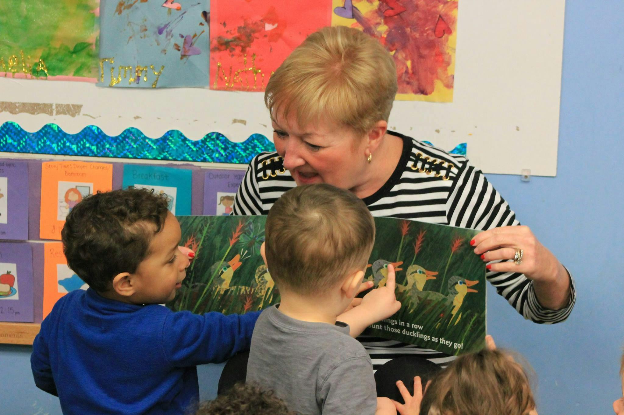Person reading a book to two children in a classroom