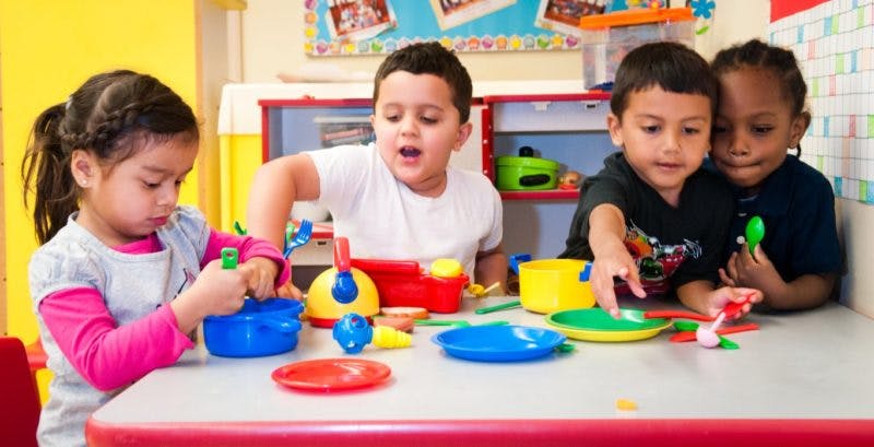 Four children playing with colorful toy dishes at a table
