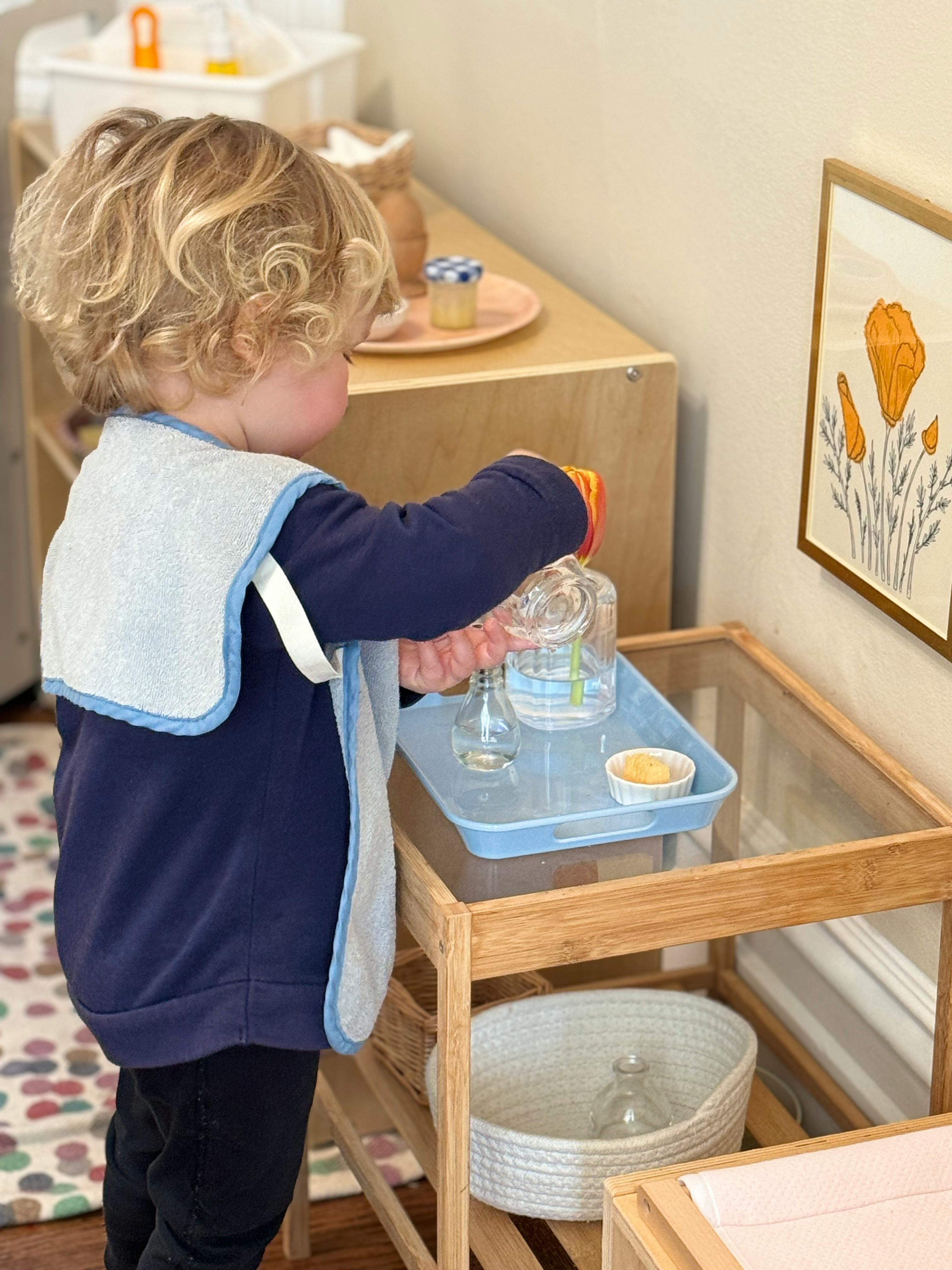 Child pouring water from a bottle into a small glass on a tray