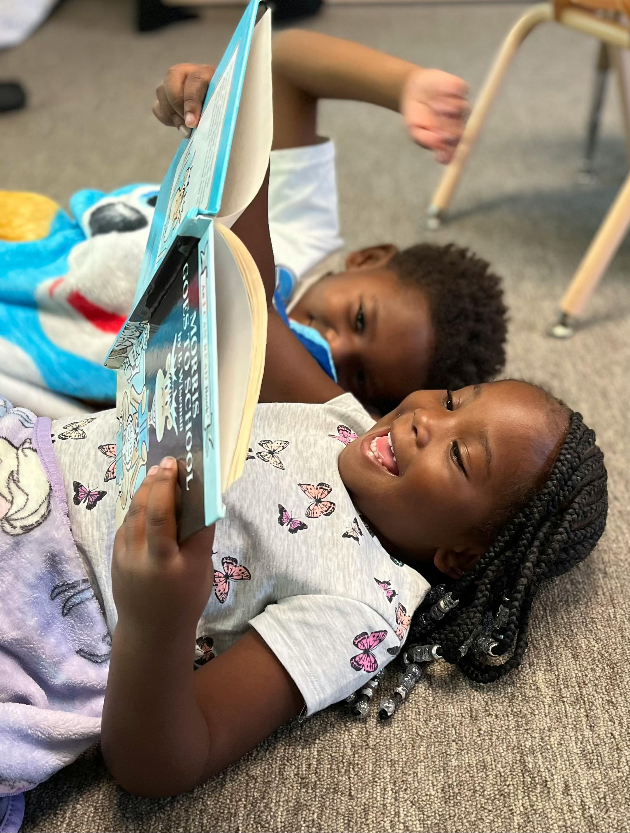 Two children lying on the floor reading a book together