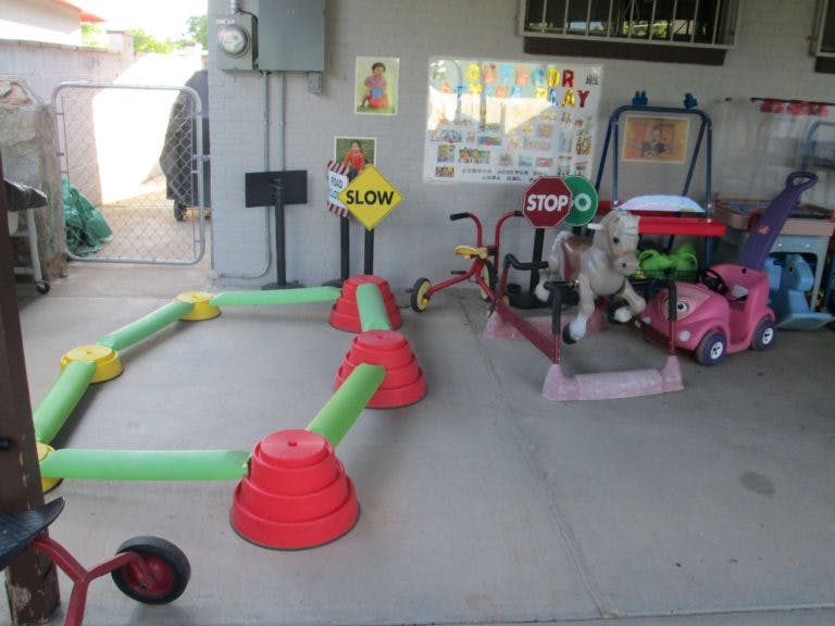 Play area with a green and red obstacle course, tricycles, and toy cars