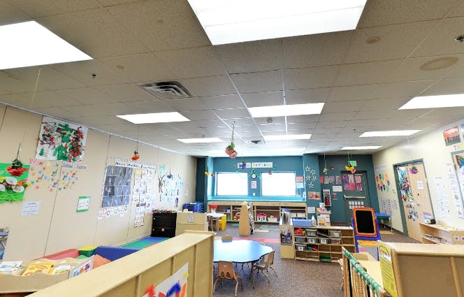 Empty classroom with tables, chairs, and children's artwork on walls