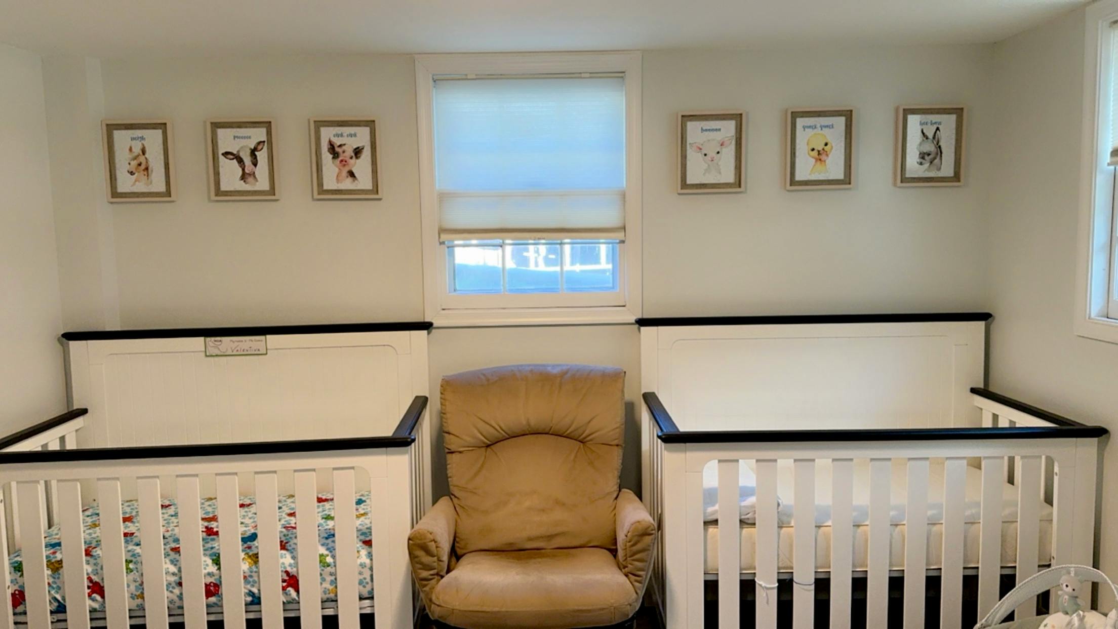 Two cribs and a recliner in a room with framed pictures on the wall