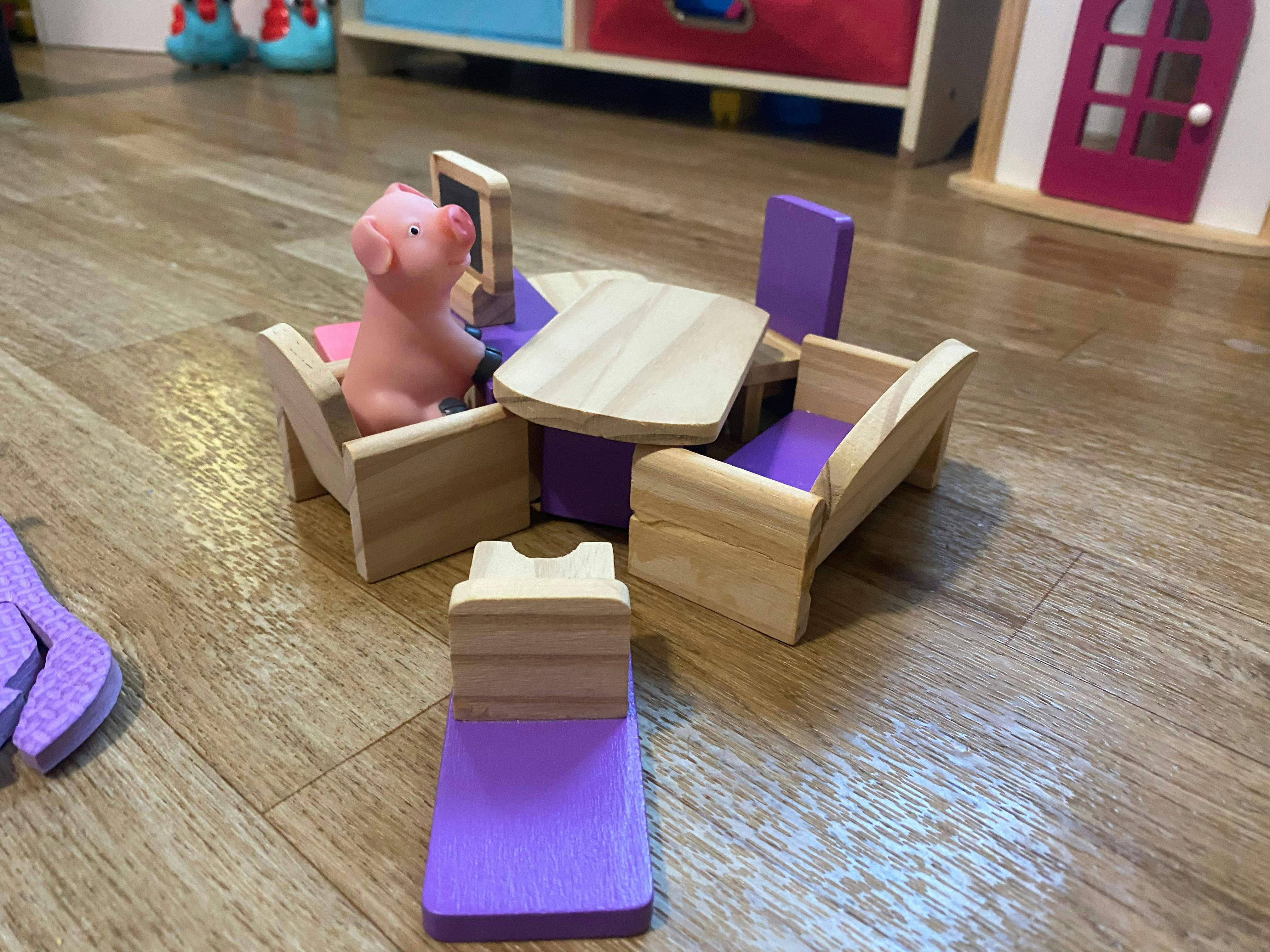 Toy pig in a wooden chair at a small wooden table with a toy computer