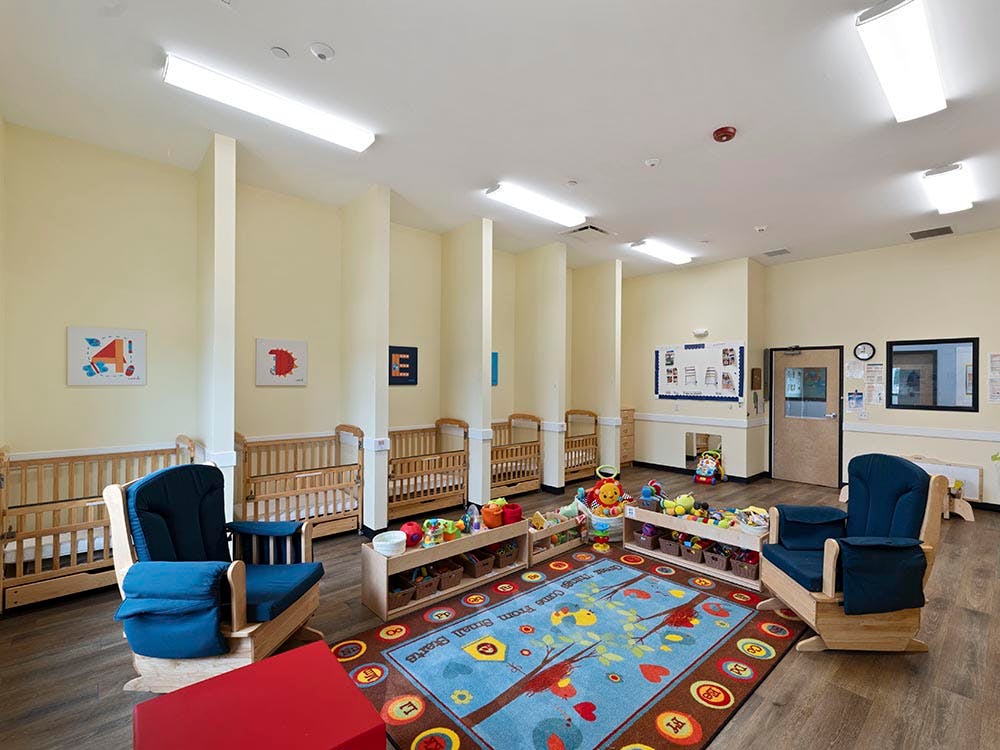 Baby room with multiple cribs, two rocking chairs, and a colorful rug
