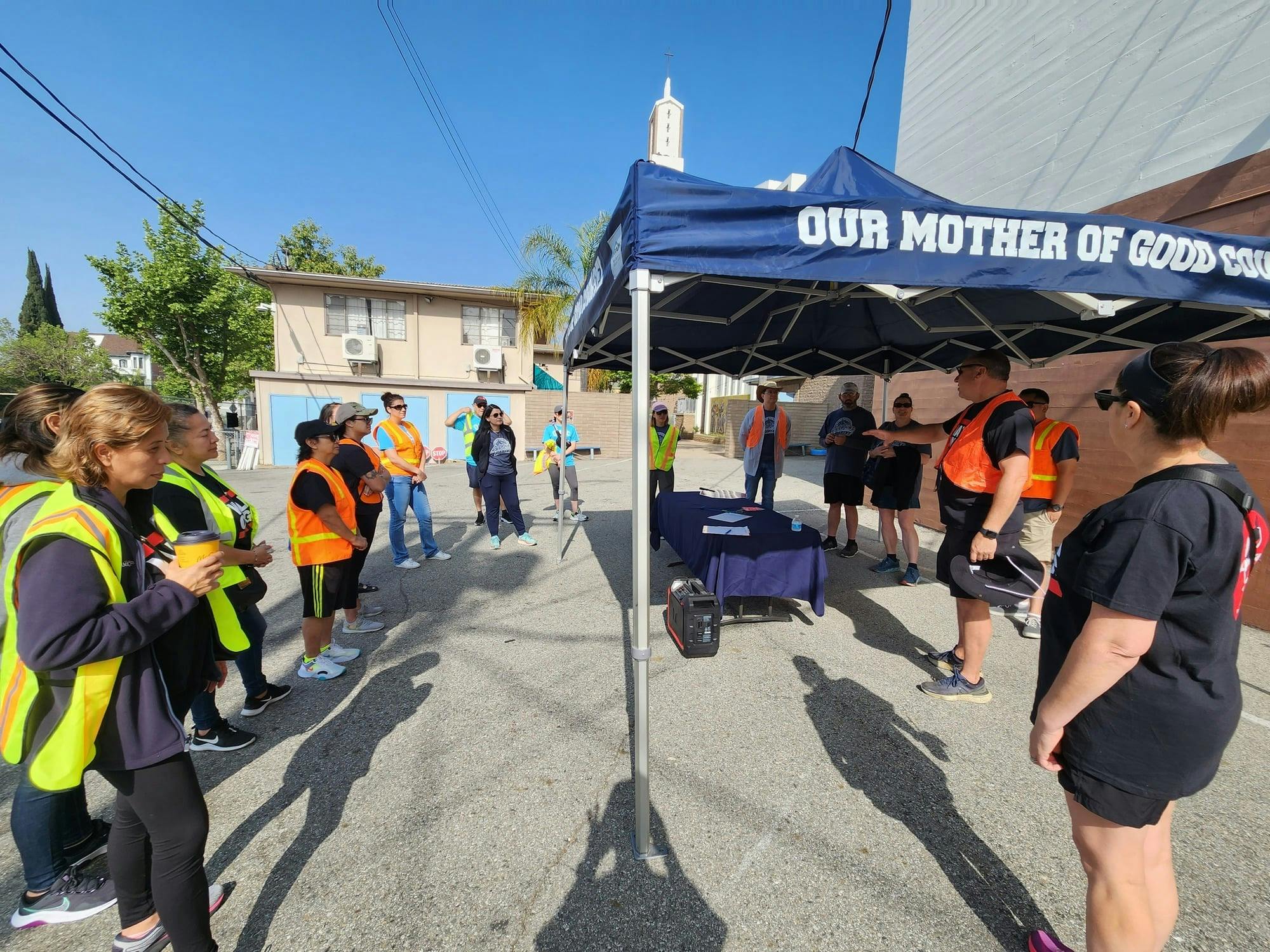 Group of people in safety vests gathered under a blue canopy