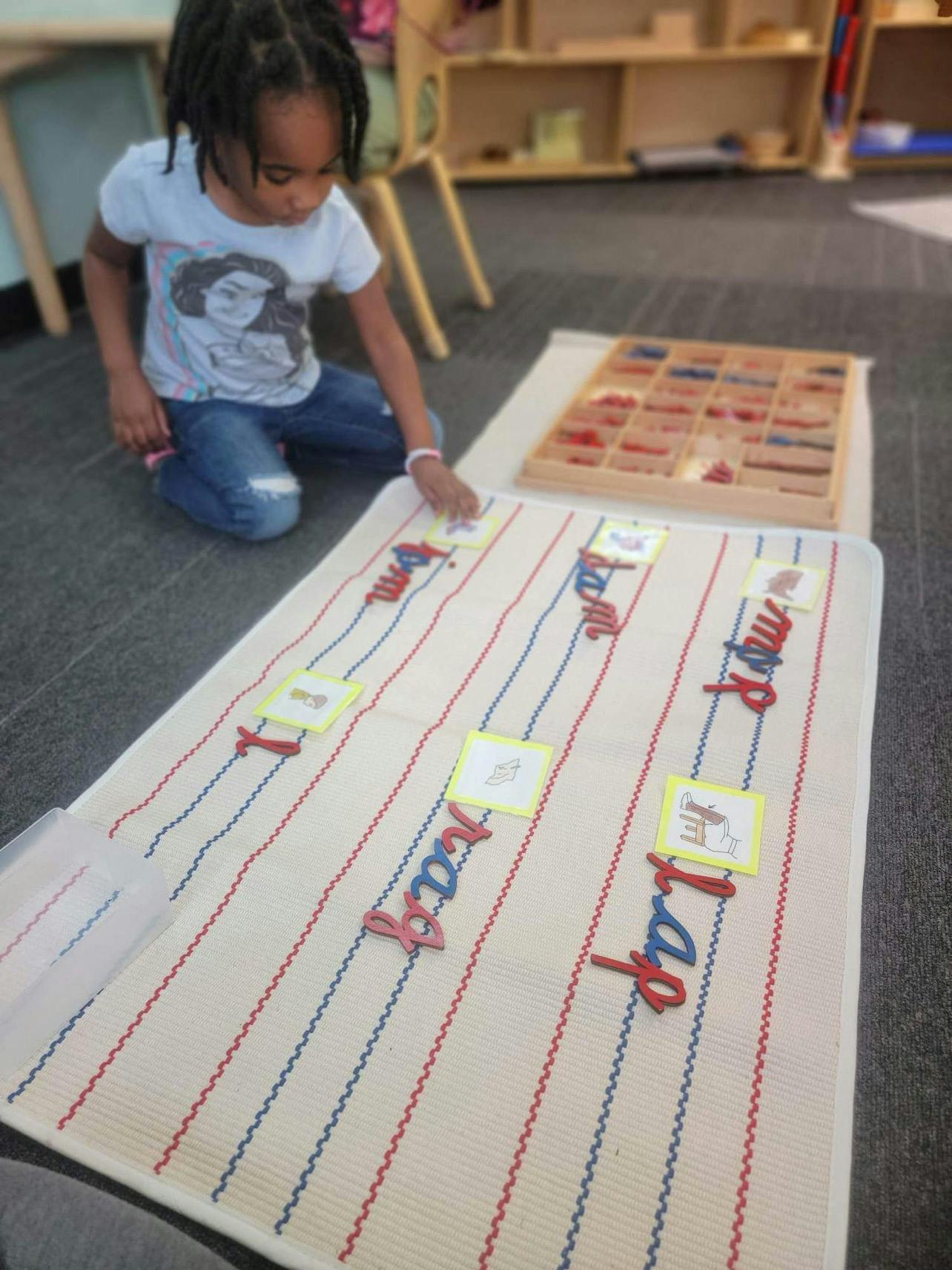 Child kneeling on floor, placing a card on a mat with words