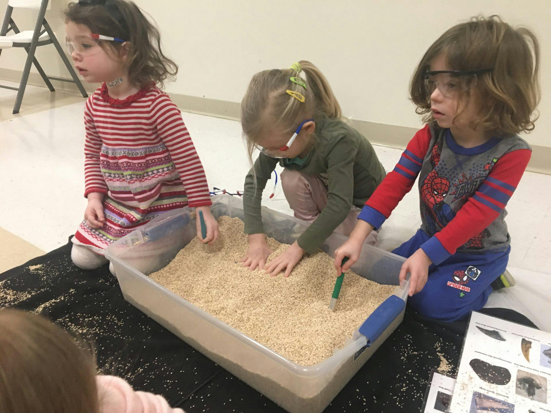 Three children playing with sand in a container