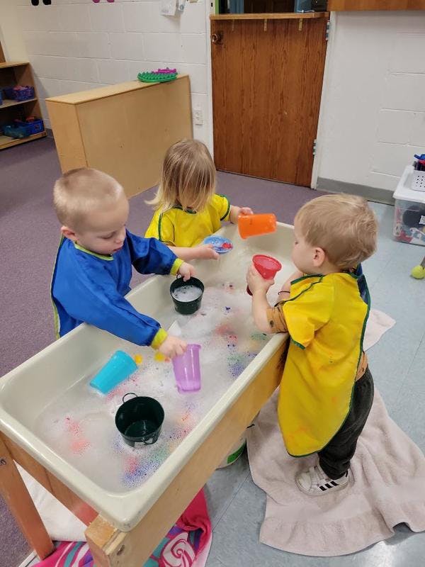Three children playing with water and cups at a sensory table