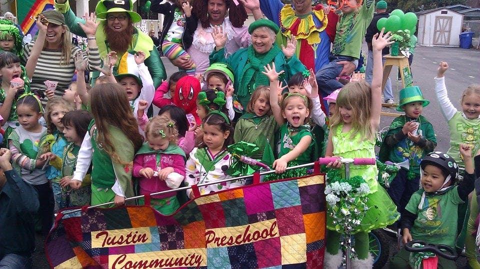 Group of adults and children in green costumes with a banner that reads "Tustin Community Preschool"