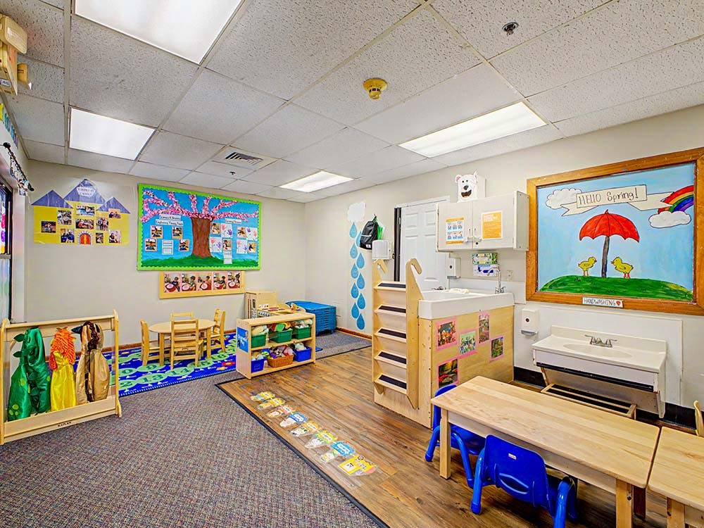 Classroom with child-sized furniture and a changing station, and a "Hello Spring!" painting