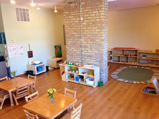 Classroom with small wooden tables and chairs, shelves with learning materials