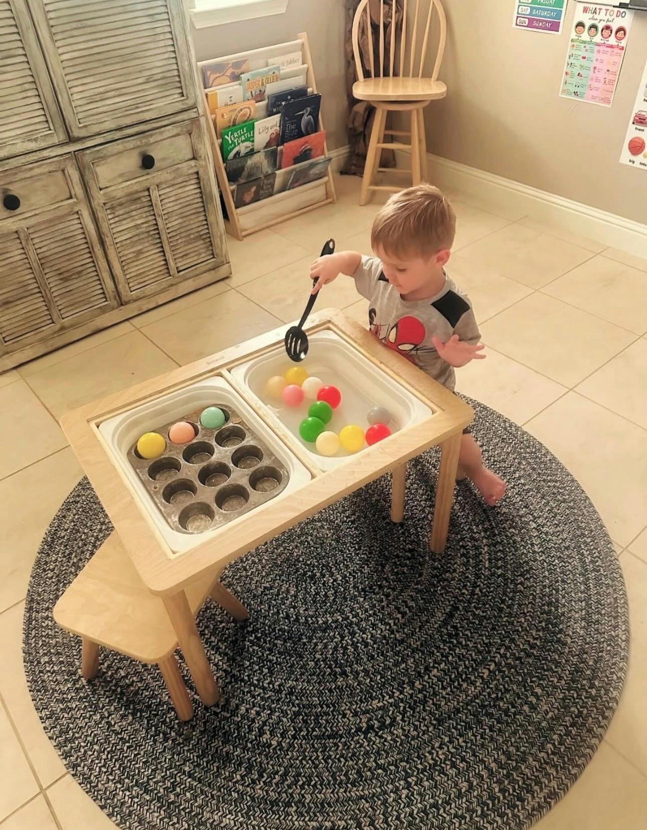 Child playing with colorful balls and a muffin tin at a small activity table