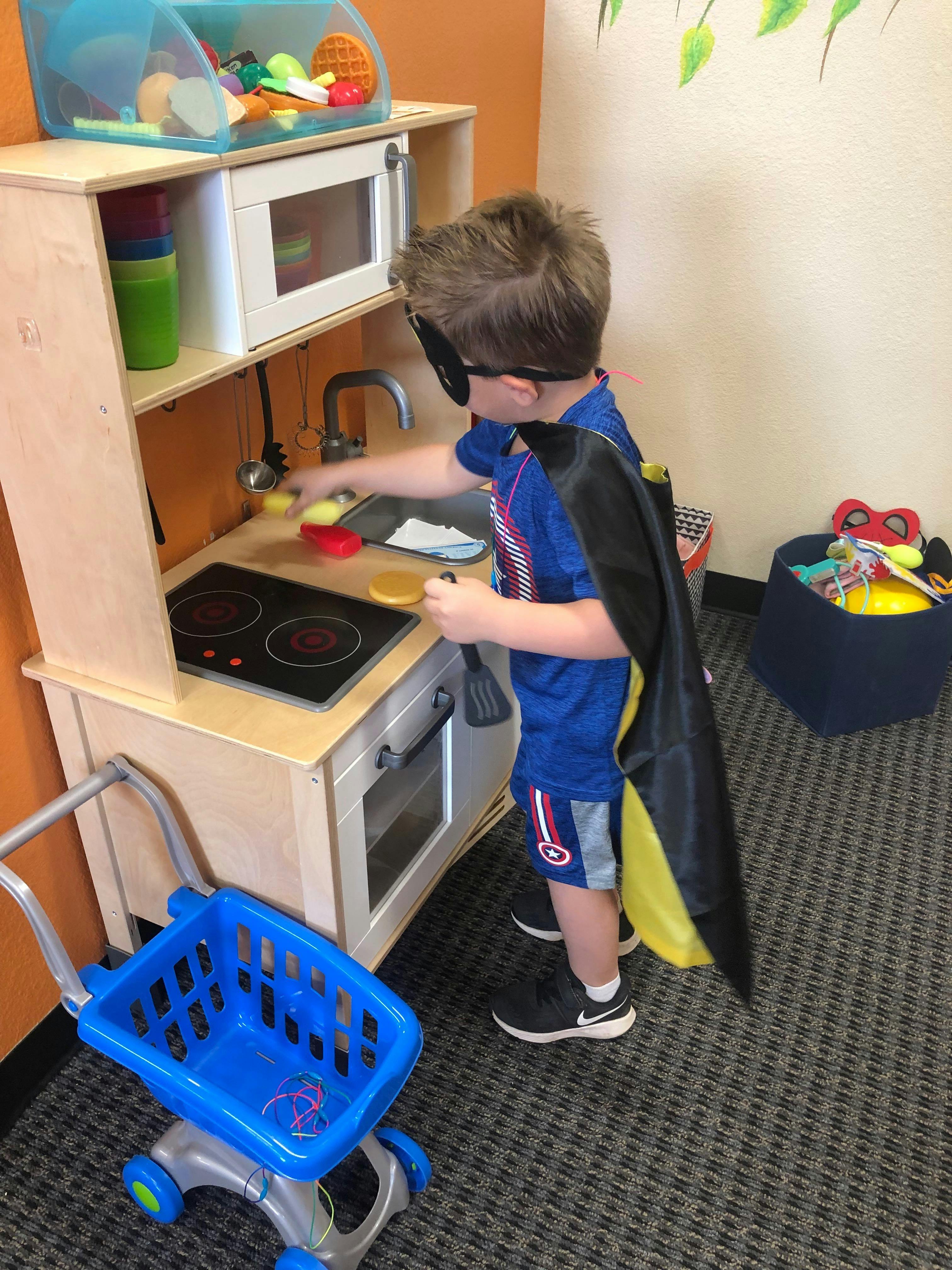 Child in a cape and mask playing with a toy kitchen
