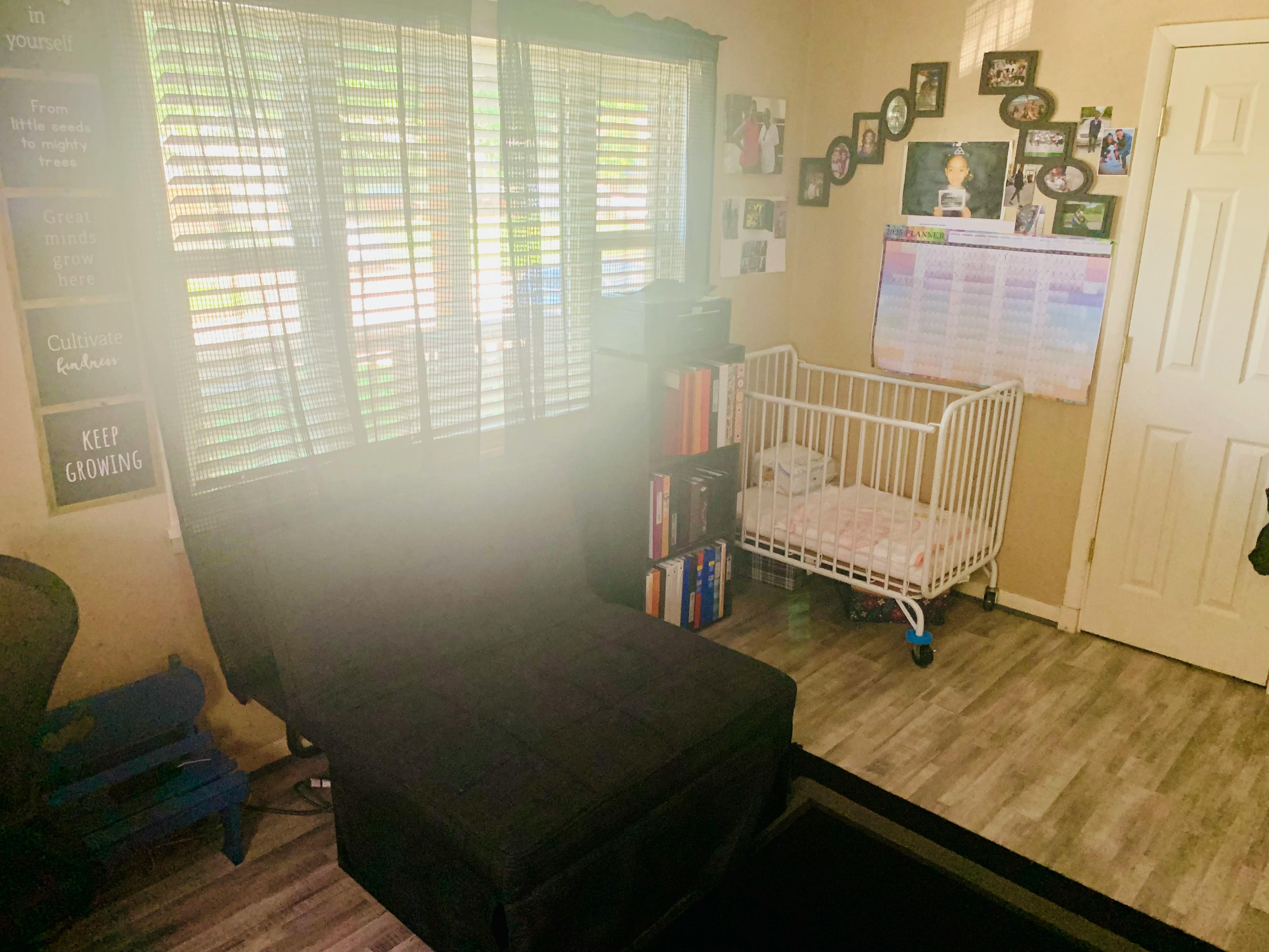Room with a black chaise lounge, white crib, and window with blinds