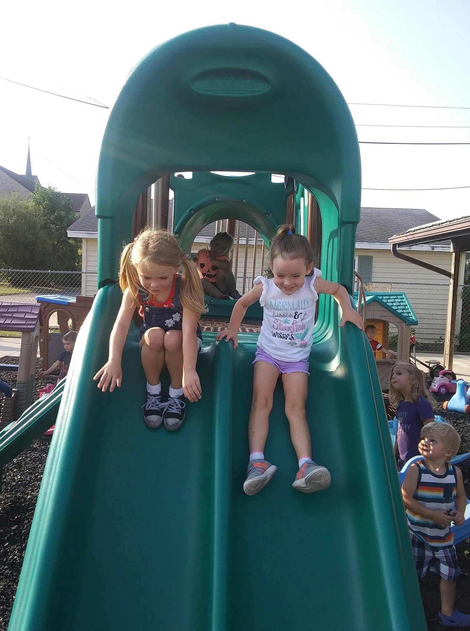 Two children on a green playground slide