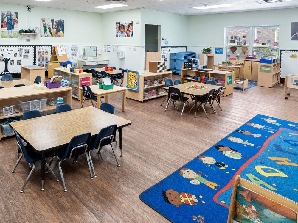 Empty classroom with small tables and chairs, and a colorful rug