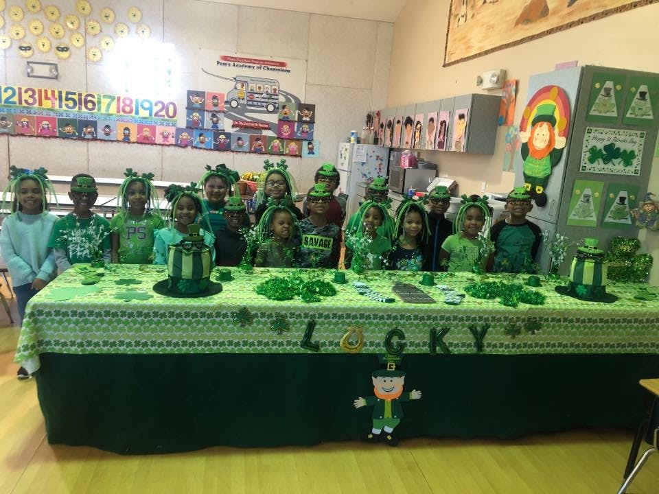 Group of children in green outfits and headbands behind a table decorated with green items