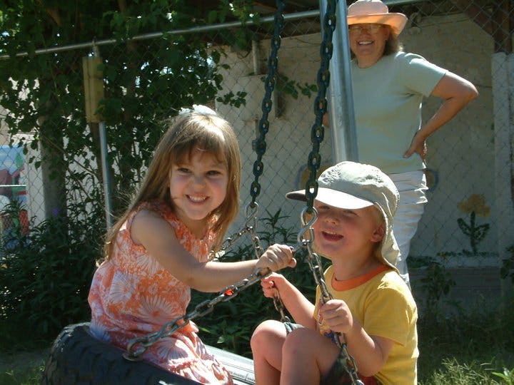Two children on swings with a person standing in the background